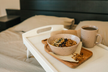 Flatlay of cozy breakfast tray with granola, milk, amber candle, and napkin on a soft beige bed. Warm tones and natural textures create a calm and peaceful morning scene