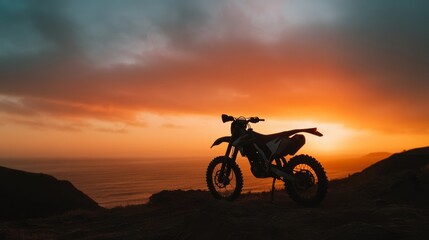 Fototapeta premium Minimal silhouette of a dirt bike parked on cliff edge during sunset, moody sky
