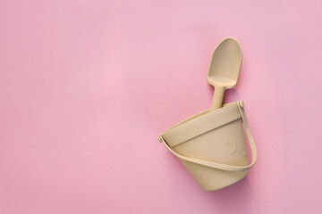 Minimalist beige silicone bucket with shovel on pastel pink background. Eco-friendly children's beach toys with modern design, flat lay composition