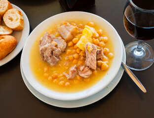 Plate with portion of hot chickpea and meat soup. First course is served with pieces of baguette..
