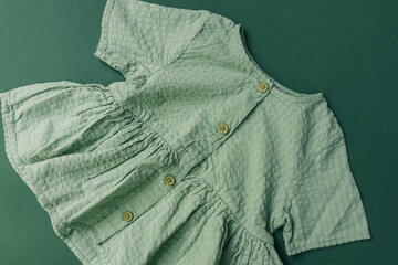 Light green cotton baby dress with wooden buttons, displayed flat on a matching green background....