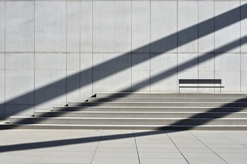 Geometric shadow patterns created by sunlight on a concrete wall and steps near a bench