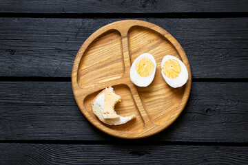 Breakfast on wooden plate, boiled eggs and bitten bread with butter and cheese