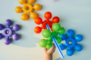 Child holding colorful interlocking plastic toys in bright blue, yellow, and red on a white background. Educational toy set for toddlers promoting creativity and motor skills
