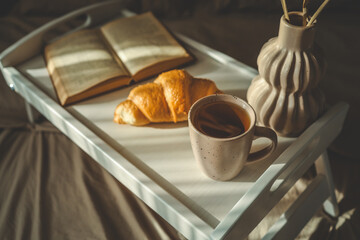 Beautiful morning scene with a croissant, candle, coffee, open book, and decorative vase on a white...