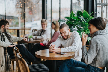 Friendly group of individuals gathered at a cozy cafe, sharing stories and laughter. Natural lighting and lush greenery enhance the relaxed and inviting atmosphere of their casual meet up.