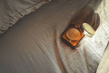 Amber glass candle with open lid placed on soft beige bedding in warm natural light, creating a minimalist and cozy composition ideal for peaceful mornings