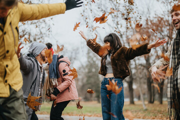 Fototapeta premium A joyful group of friends enjoying an autumn day outdoors by playing in falling leaves. The image conveys happiness, friendship, and the beauty of nature during the fall season.