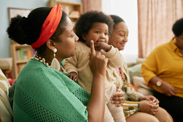 Side view of African American mother holding child while meeting with family in cozy living room