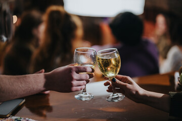 Two people clinking glasses of sparkling wine together with a festive background atmosphere, symbolizing celebration, friendship, and enjoyment during a social gathering with a warmly lit ambiance.