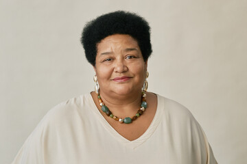 Portrait of mature African American woman with short curly hair wearing beaded necklace and white top, smiling softly at camera in studio