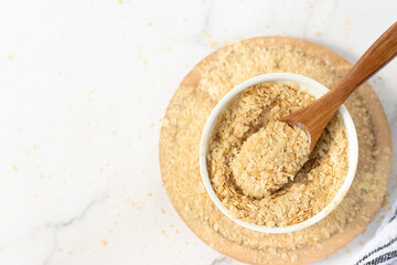 Nutritional yeast flakes in a bowl with wooden spoon on white kitchen table. Top view. Copy space.