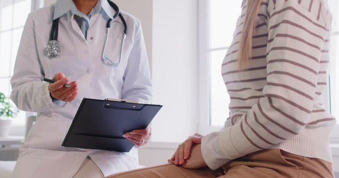 Portrait of female doctor talking with young patient sitting on couch in clinic. Physician giving consultation a woman during medical examination in office. Medicine and treatment concept. 4k video.