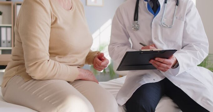 Faceless doctor in white coat and woman patient sitting on couch, writing down recommendations for curing disease after checkup or prescription, holding clipboard with medical report