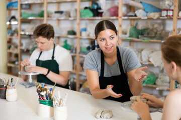 Potter helps young apprentices mold pottery from clay in a workshop