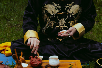 Male shaman or Wu wearing embroidered kimono conducting Chinese tea ceremony outdoors