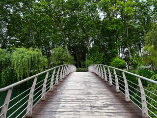 Fototapeta premium Wooden pedestrian bridge surrounded by lush tree foliage in a forest park