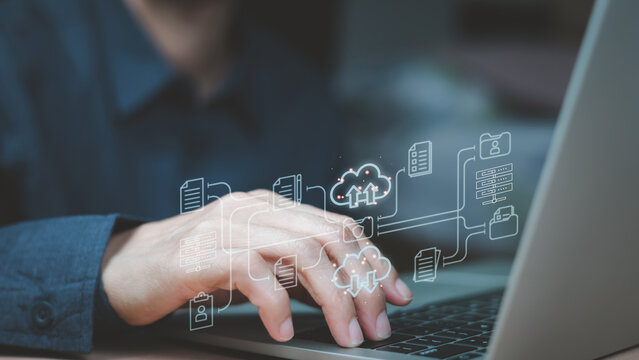 Businessman hands interacting with a laptop keyboard, overlaid with glowing digital icons representing cloud computing and data management.Online documentation database and process automation. (DMS).