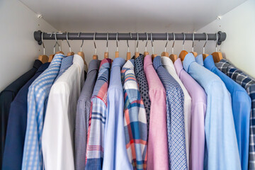 Neatly arranged men shirts hanging on wooden hangers in wardrobe. Minimalist clothing organization...