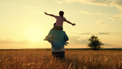 Happy family dad kid playing pilot in field. Kid on dad shoulders, holding hands, in field with ripe wheat. Dad run through field with ears wheat, holding daughter on shoulders. Concept kids dream fly