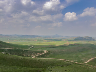  Vast panoramic view of winding roads through lush green hills under a cloudy sky, Kyrguzstan