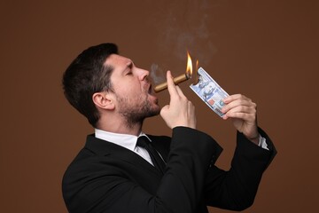 Greedy banker lighting cigar with dollar banknote on brown background