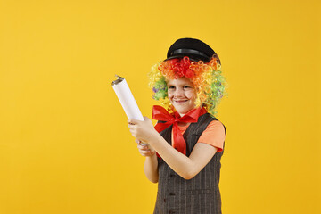 Happy little boy dressed like clown with confetti popper on yellow background. Surprise party