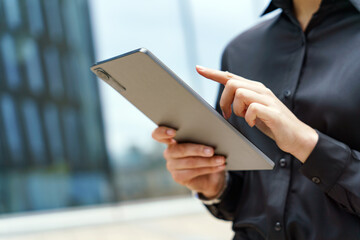 Professional in business attire engages with a tablet outdoors in a modern urban setting during...