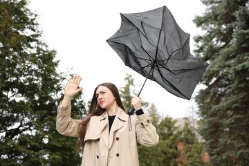 Woman with broken umbrella fighting wind outdoors, low angle view