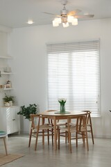 Wooden table, chairs, tulips and green houseplants near window indoors. Interior design
