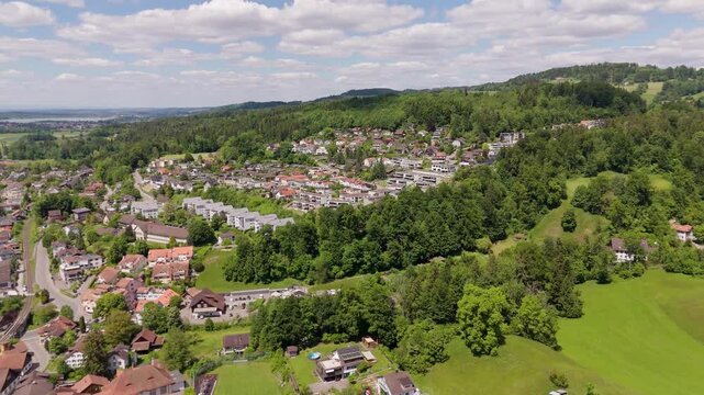 Aerial establishing shot of luxury swiss city on hillside with green trees. CLouds at sky in summer. Wide shot. Homes and houses in noble district.