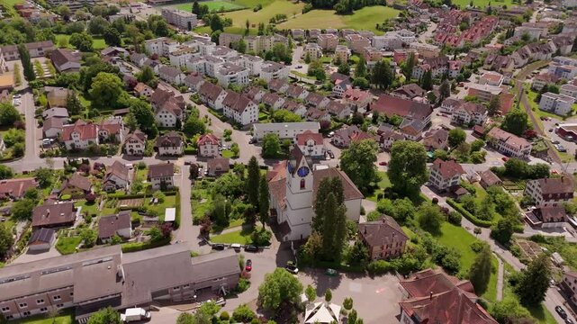 Historic church tower in Hinwil a swiss town in summer. Aerial top down orbit shot. Red roofs of houses and luxury apartment Blocks in Switzerland. Green grass and trees.