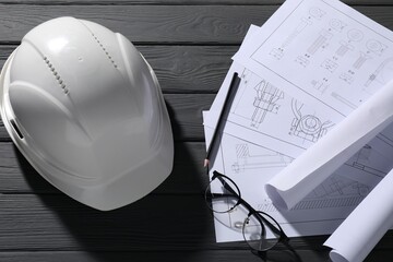 Different engineering drawings, hard hat, glasses and pencil on grey wooden table, flat lay