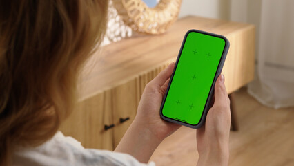 Woman sit use digital tech cell phone with green screen mock up. Hand scroll phone web site, swipe like photos. Girl hold mobile closeup. Chroma key page. Cozy home background. Online app copy space.