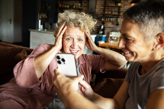 Senior lesbian couple laughing and reacting to funny video on smartphone at home