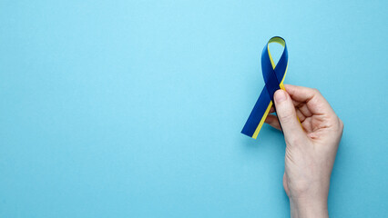 A person holds a yellow and blue awareness ribbon, symbolizing World Down Syndrome Day