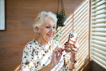Senior woman smiling during a video call on smartphone at home in sunlight
