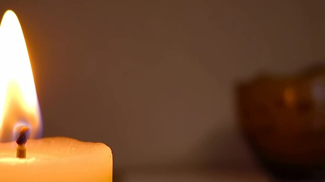 Close up shot of a lit wax candle flame and soft light, creating a warm and relaxing ambiance in an interior setting.
