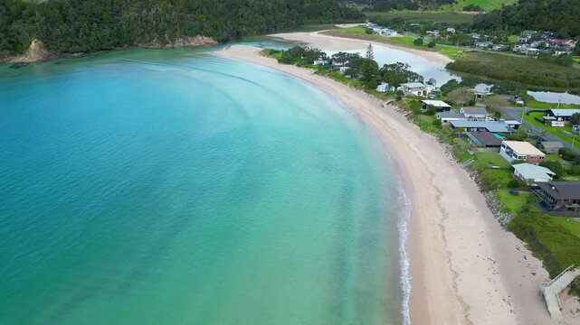 Sweeping drone footage of traditional baches lining a pristine beach and calm sea in coastal New Zealand. Matapouri.