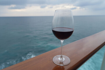 Intriguing crimson wine glass poised over tranquil ocean waves, whispers of Mediterranean escape, celebrating Bacchanalia and Ocean Day
