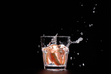 Dentures falling into glass of water with splash, black background with copy space