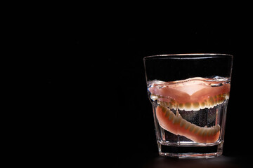 Dentures falling into glass of water with splash, black background with copy space