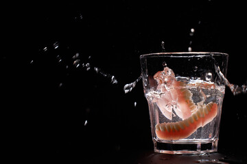 Dentures falling into glass of water with splash, black background with copy space