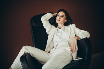 Confident businesswoman in a white suit posing elegantly in an armchair with a professional...