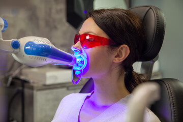 Dental procedure of laser teeth whitening, woman wearing red safety glasses and special mouthpiece.