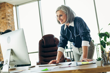 Elegant mature businesswoman working confidently at her office desk with a modern white computer in a corporate setting
