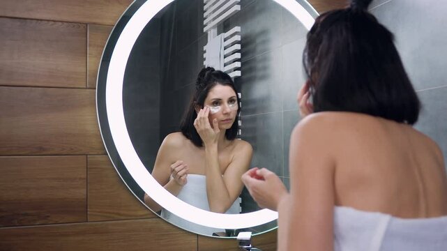 Woman in white towel round her body which putting patches under eyes for fresh look