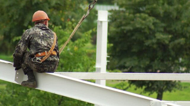 A male fitter at a construction site assembles a metal structure at a construction site in the summer. Danger at height, copy space for text