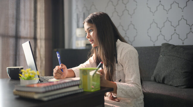 Indian young adult female girl doc nurse use laptop look screen talk speak on distant patient video call. doctor staff do online health care work writing medicine prescription home office clinic job