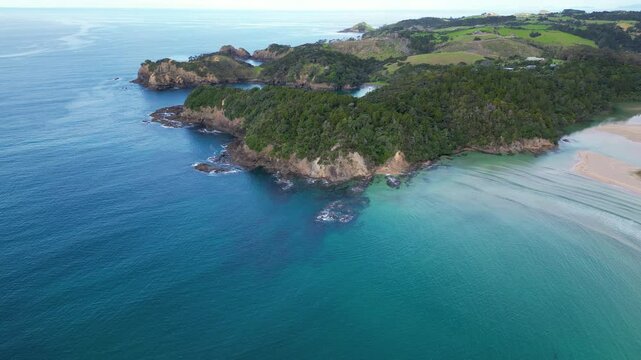 Drone view of untouched coastline, blue sea, and lush greenery near Matapouri in Northland, New Zealand.